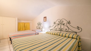 Ein Zimmer mit zwei Betten, jedes mit gestreifter Bettwäsche, einem kleinen Nachttisch mit Lampe und einem Bild an der Wand.
