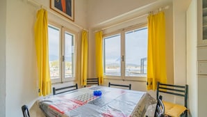 Ein Esszimmer mit einem Tisch, der mit einer Tischdecke bedeckt ist, gelben Vorhängen an den Fenstern und Blick auf die Stadt und die Berge.