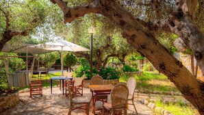 Eine Terrasse im Freien mit Steinböden, Korbmöbeln und einem Tisch unter einem großen Sonnenschirm.