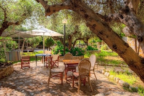 An outdoor patio with stone flooring, wicker furniture, and a table under a large umbrella. - Villa Melina - Four Bedroom Villa, Sleeps 8 (Tavronitis)