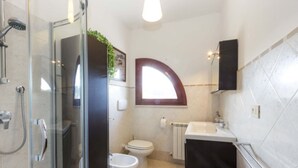 Et badeværelse med glasbrusekabine, toilet, håndvask og et håndklædetørrestativ.