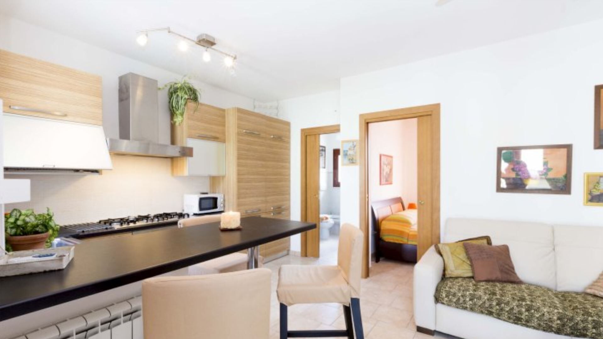 Eine moderne Küche mit einer zentralen Kochinsel, einer Mikrowelle und einem Herd. Es gibt einen Essbereich mit Tisch und Stühlen. Der Raum verfügt über ein weißes Sofa und ein Bett mit bunter Bettwäsche.
