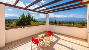 En balkong med en träpergola, två röda stolar, ett litet bord och utsikt över berg och träd.