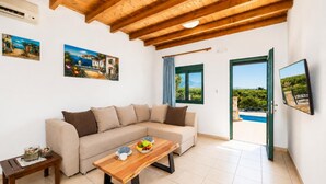 Una sala de estar con un sofá, una mesa de centro con fruta, un televisor y vista a una piscina.