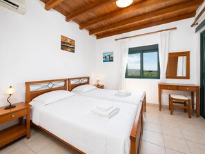 A bedroom with two beds, a desk, a chair, a window with a view, and a ceiling fan.