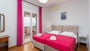 A double bed with a red bedspread, a bedside table, a nightstand, a mirror, a window with pink curtains, and a ceiling light. - Michalis - Three Bedroom Villa, Sleeps 6 (Nisaki)