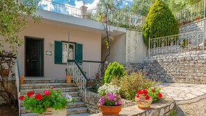 A stone staircase leading to a house with a balcony, surrounded by potted plants and flowers. - Michalis - Three Bedroom Villa, Sleeps 6 (Nisaki)