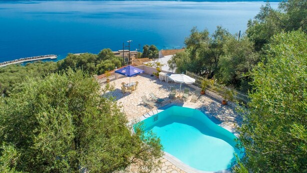 A pool area with a view of the sea, surrounded by trees and a stone patio. - Michalis - Three Bedroom Villa, Sleeps 6 (Nisaki)