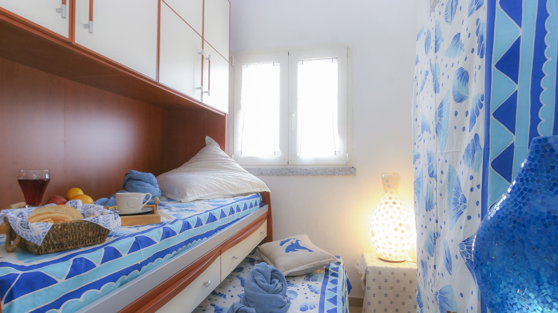 Ein kleines, ordentlich eingerichtetes Schlafzimmer mit Bett, Nachttisch und Fenster.