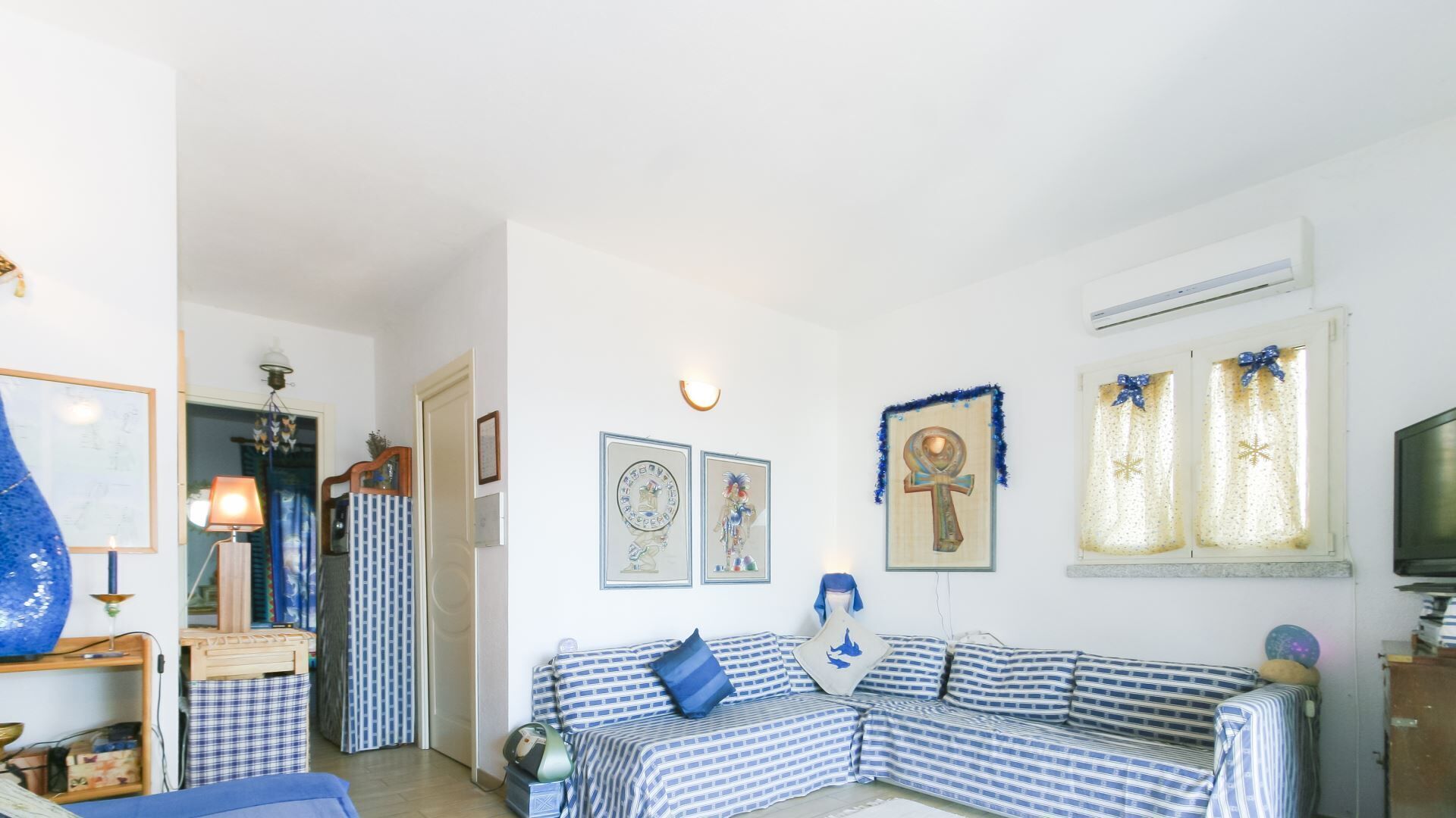 Ein Wohnzimmer mit einem blau-weißen Karosobereich, einem Fernseher und gerahmten Kunstwerken an den Wänden.