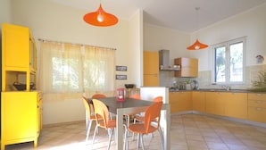 A bright kitchen with yellow cabinets, a dining area with orange chairs, and pendant lights. - Villa Asteria directly on the beach (Campo nell'Elba)