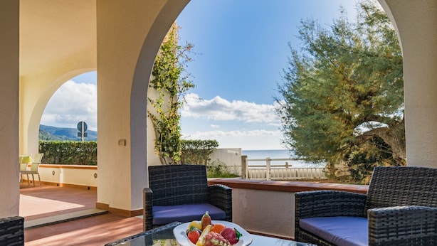 A terrace with wicker furniture, a table with fruit, and a view of the sea and hills. - Villa Asteria directly on the beach (Campo nell'Elba)