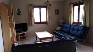A living room with a television, sofa, coffee table, and windows with curtains. - Le Vignal 2, cottage with 2 bedrooms in the south of the Ardèche (Chambonas)