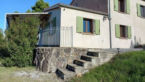A two-story house with a stone staircase leading to the entrance, a balcony with a metal railing, and green shutters on the windows. - Le Vignal 2, cottage with 2 bedrooms in the south of the Ardèche (Chambonas)
