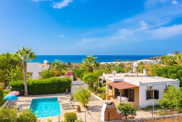 A pool with a view of the sea, a white building with a red roof, and a clear blue sky. - Villa Eleni - Two Bedroom Villa, Sleeps 5 (Kissonerga)