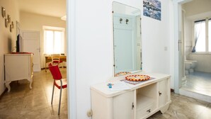 Una habitación con un tocador blanco, un espejo, una silla roja y una pequeña mesa con un objeto colorido encima.