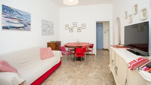 Un espacio habitable compacto con comedor, sofá, televisor y una pequeña cocina.