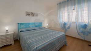 Une chambre à coucher avec une couvre-lit à rayures bleues, des tables de chevet blanches et une fenêtre ornée de rideaux bleus.