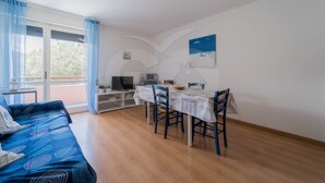 Une pièce comprenant un canapé, une table à manger avec des chaises, un téléviseur et un balcon avec vue.