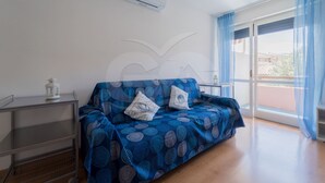 Une pièce avec un canapé bleu à motifs, une petite table sur laquelle est posée une lanterne blanche, et une grande fenêtre ornée de rideaux bleus.