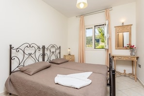 Ein Schlafzimmer mit Bett, Nachttisch, Kommode, einem Fenster mit Vorhängen und einem Spiegel.