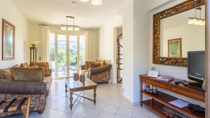 Un salón espacioso con un televisor grande, una mesa de centro de madera y dos sofás. Hay un espejo grande en la pared y una escalera que lleva a un balcón.