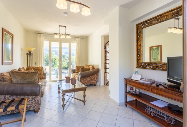 Ein geräumiges Wohnzimmer mit großem Fernseher, einem Holztisch und zwei Sofas. An der Wand befindet sich ein großes Spiegel, und eine Treppe führt zu einem Balkon.