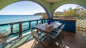 Una terraza con mesa y sillas de madera, con vista a un cuerpo de agua y una costa distante.