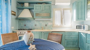Una cocina con armarios color turquesa, una estufa y un microondas. Hay una mesa de comedor con sillas y un mantel azul.