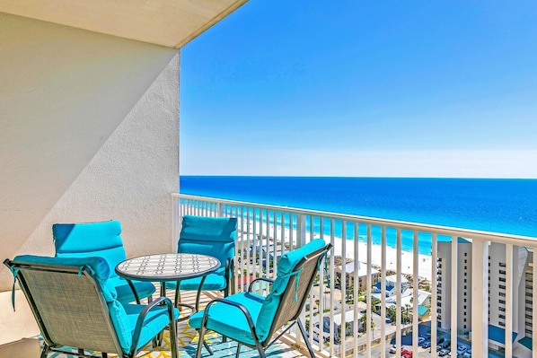 Ein Balkon mit Tisch und Stühlen, der Blick auf einen Strand und ein Wohngebiet freigibt.