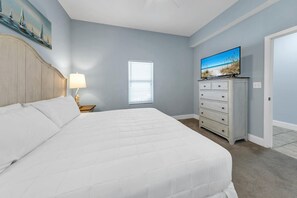 Ein Schlafzimmer mit einem großen Bett, einem Schminktisch, einem Fernseher und einem Fenster mit Jalousien.