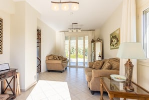 A spacious living area with two sofas, a coffee table, and a lamp. There is a staircase leading to a balcony with a view of greenery.