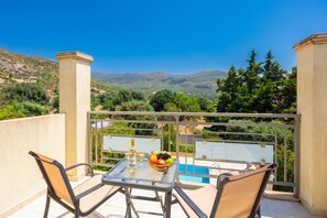 Un balcon avec une table et des chaises, une bouteille de vin et un saladier de fruits.