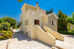 A two-story building with a staircase leading to the entrance, a swimming pool, and a landscaped garden.