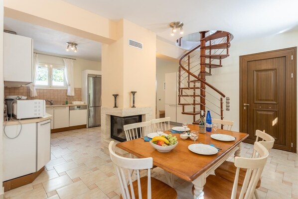 Una cocina moderna con comedor, una escalera espiral y una gran mesa de madera dispuesta para una comida.