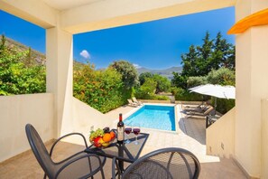 A balcony with a pool, outdoor furniture, and a table with a bottle of wine and fruit.