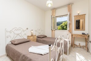 A bedroom with two beds, a wooden dresser, a mirror, and a window with a view of greenery.