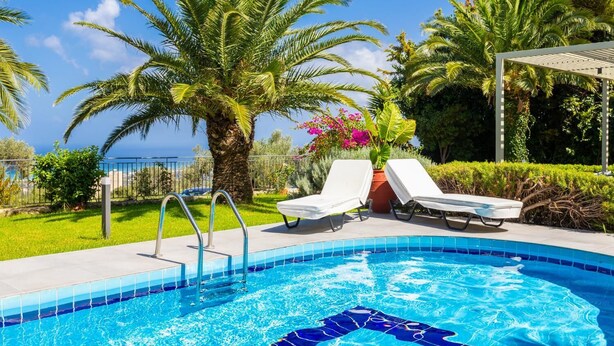 A swimming pool with two lounge chairs, a palm tree, and a view of the sea. - Villa Sevos - Two Bedroom Villa, Sleeps 4 (Crete)