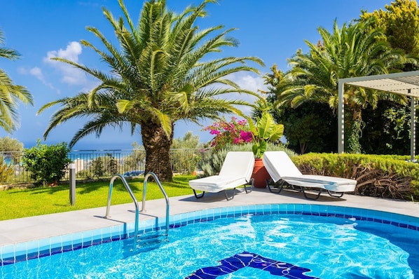 A swimming pool with two lounge chairs, a palm tree, and a view of the sea. - Villa Sevos - Two Bedroom Villa, Sleeps 4 (Crete)