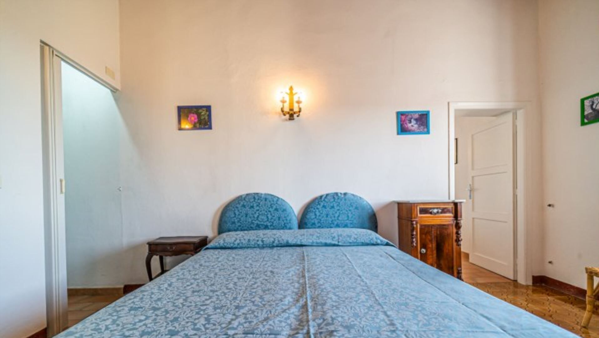 Ein Schlafzimmer mit einem Bett, einem Nachttisch, einer Wandleuchte und zwei gerahmten Bildern.