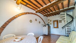 Un coin repas avec une table ronde et des chaises, une arche en briques, un escalier et une petite fenêtre avec des rideaux.