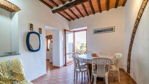 Un coin repas avec une table ronde et six chaises, un motif circulaire bleu sur le mur, et une vue sur l’extérieur à travers une porte vitrée.