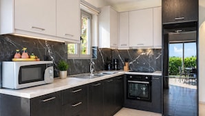 A modern kitchen with dark cabinetry, a built-in oven, a microwave, and a window.