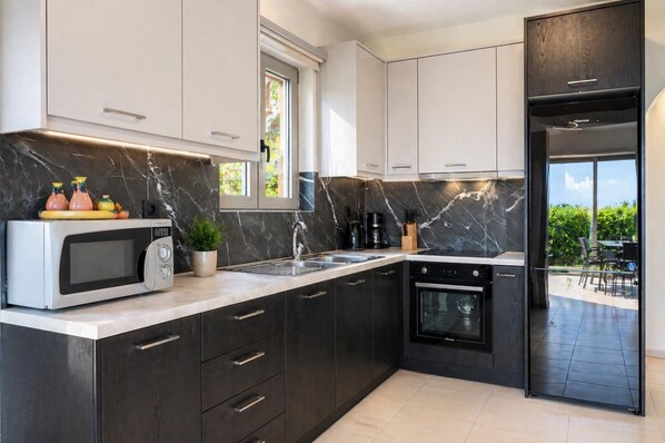 Una cocina moderna con armarios oscuros, horno empotrado, microondas y una ventana.