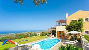 A swimming pool with lounge chairs, a slide, and a view of the sea.