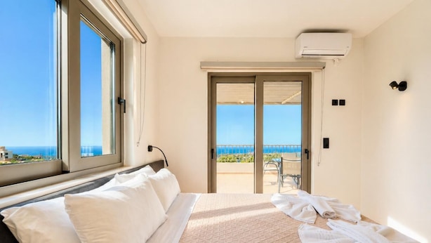 A hotel room with a bed, a view of the sea, a balcony, and an air conditioning unit.