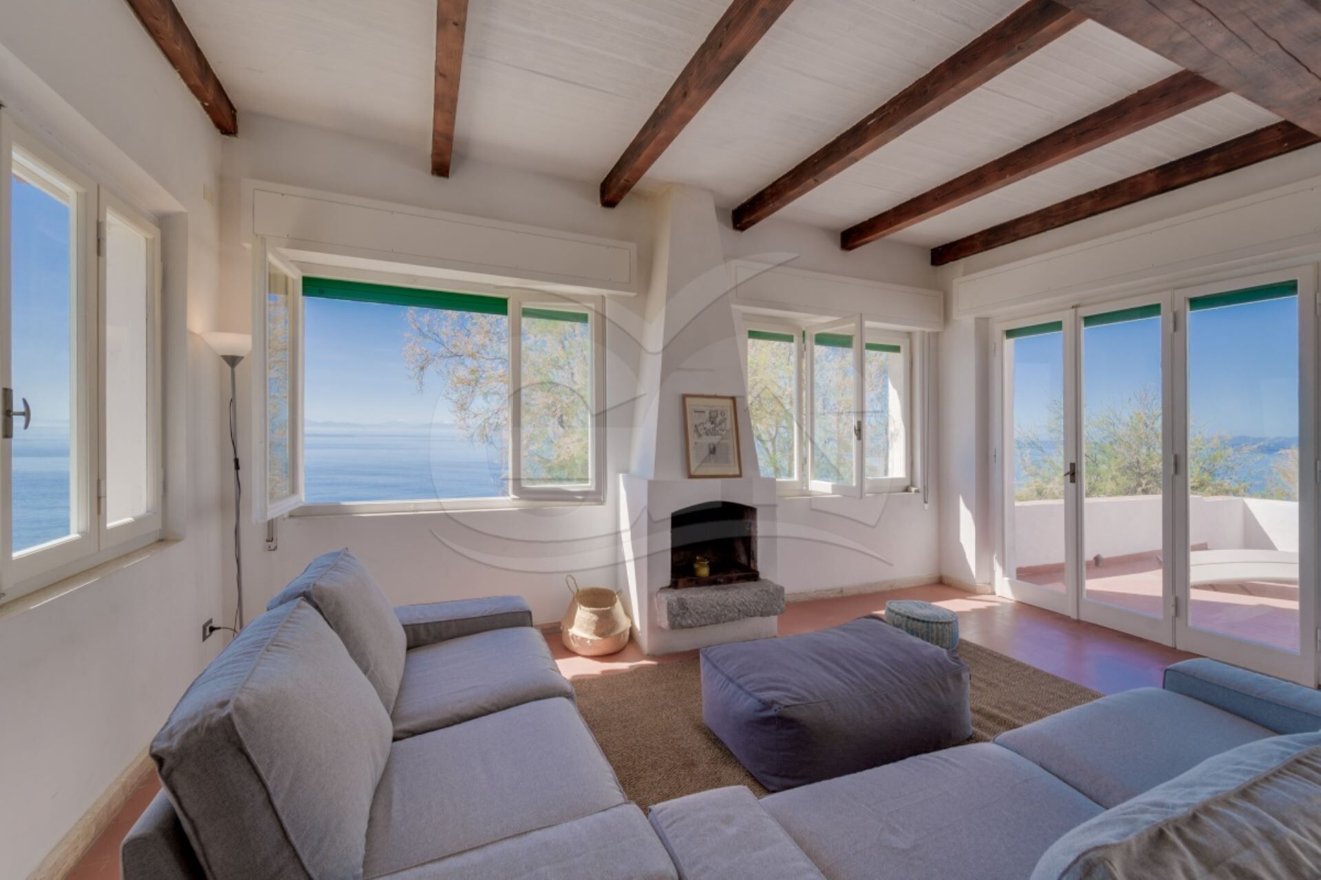 Un salón amplio con chimenea, ventanas grandes y vista al mar.