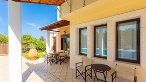 A covered patio with a table and chairs, a large potted plant, and a view of a swimming pool. - Villa Kefalas Large Private Pool, A/C, WiFi (Apokoronos)