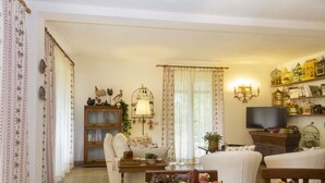 A cozy living room with a sofa, a wooden cabinet, a television, and decorative birdcages. - Villa Monserrato with garden and sea view (Porto Azzurro)