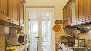 A compact kitchen with wooden cabinets, a microwave, a washing machine, and a sink. - Villa Monserrato with garden and sea view (Porto Azzurro)